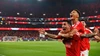 Zwei Benfica-Profis jubeln ausgelassen huckepack auf dem Rasen vor vollbesetzten, rot leuchtenden Rängen bei einem Abendspiel unter Flutlicht.